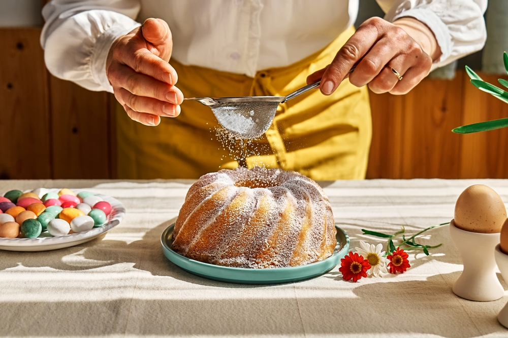 Hands dusting powdered sugar over a bundt cake