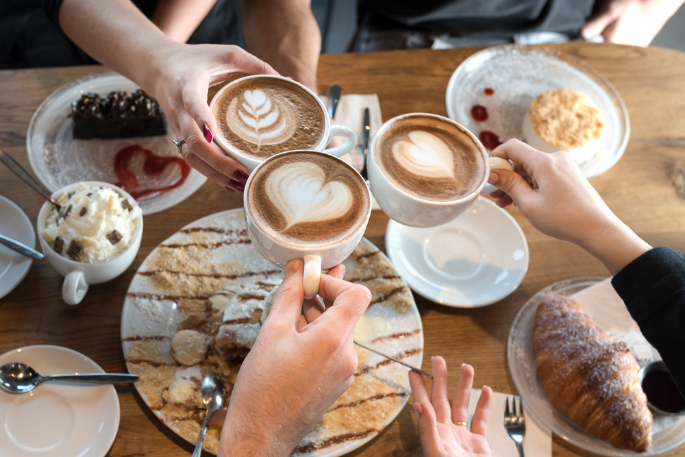Three hands holding white ceramic cups with latte art
